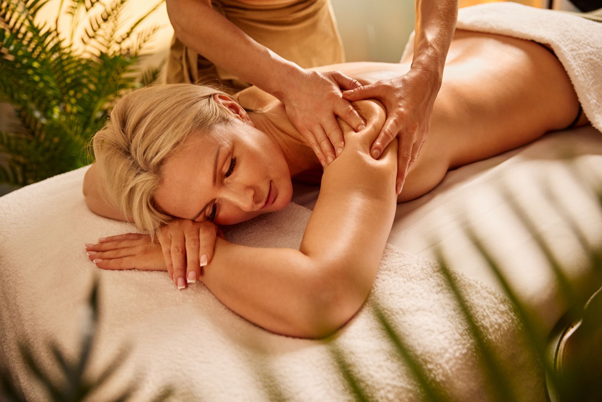 Person receiving a back massage on a spa table with soft towels and warm lighting