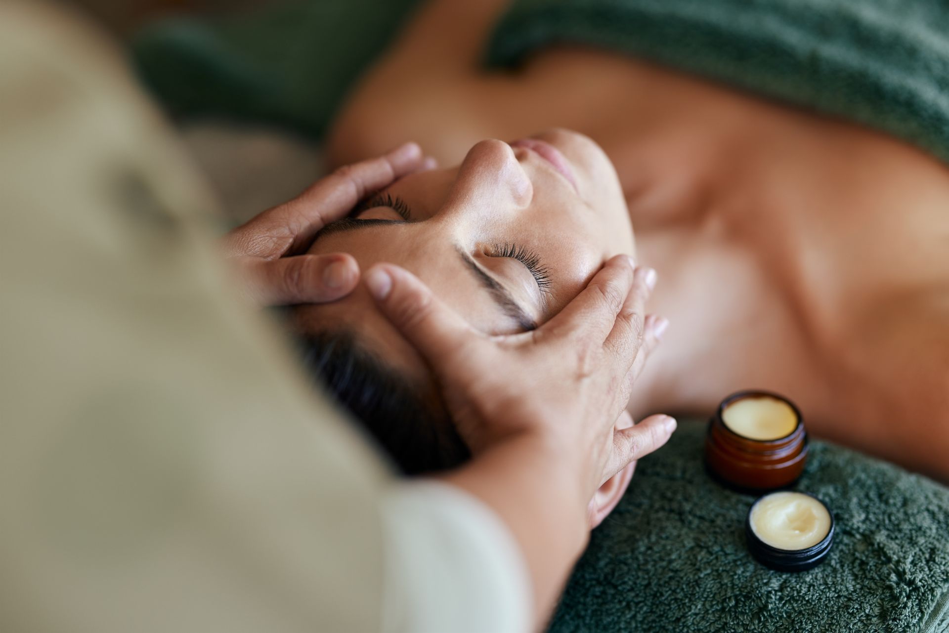 Close-up of a face massage with hands and two small jars on a dark towel