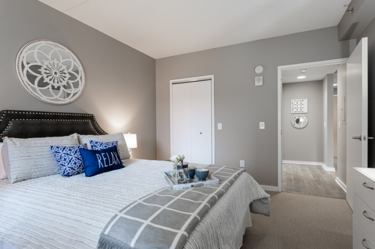 A bedroom with a bed, gray walls, and an open door leading to a hallway. The bed has white and blue bedding.