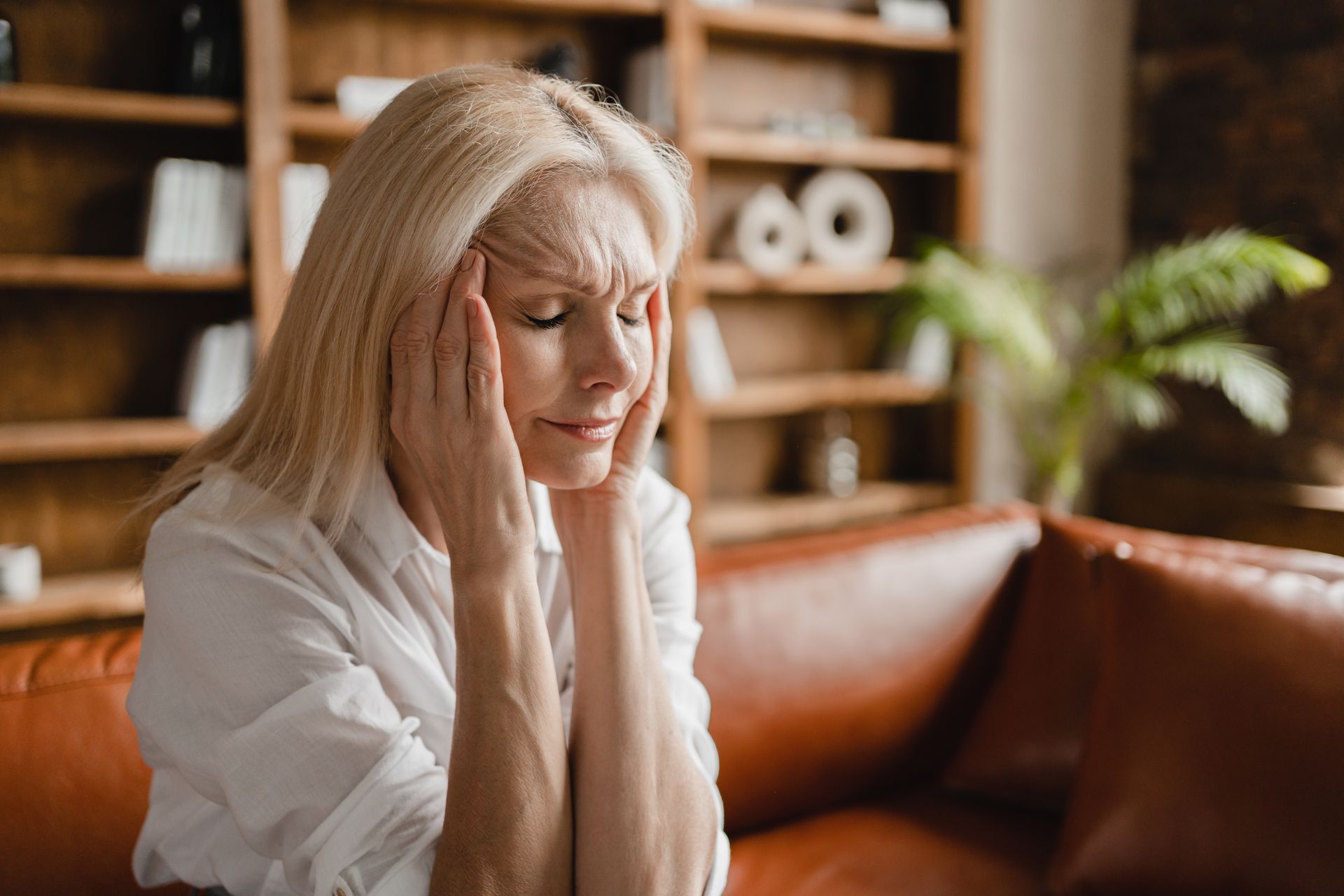 Woman sitting on a leather couch with hands on her face, looking distressed in a cozy living room