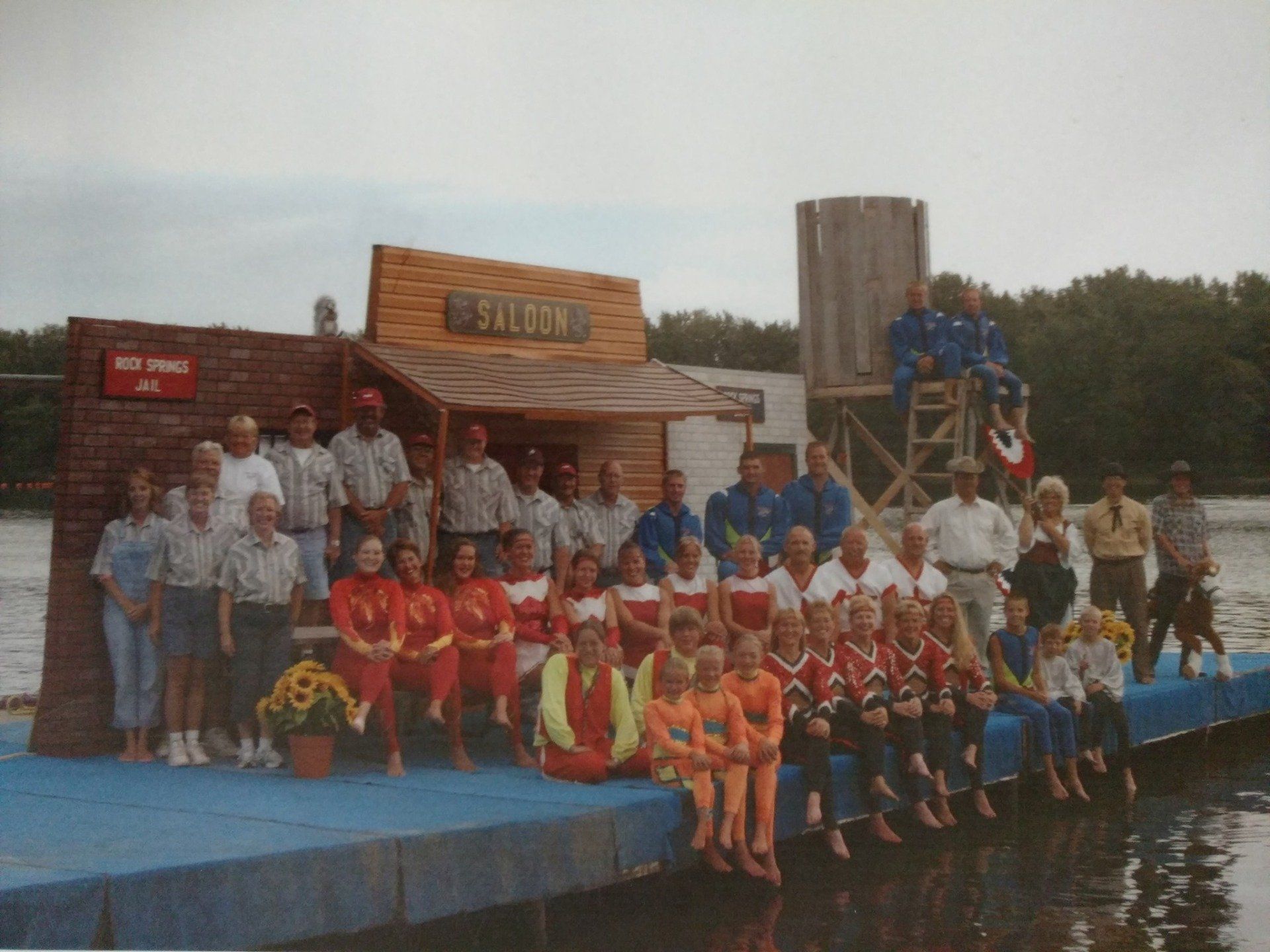 A group of people standing on a dock in front of a building that says Saloon