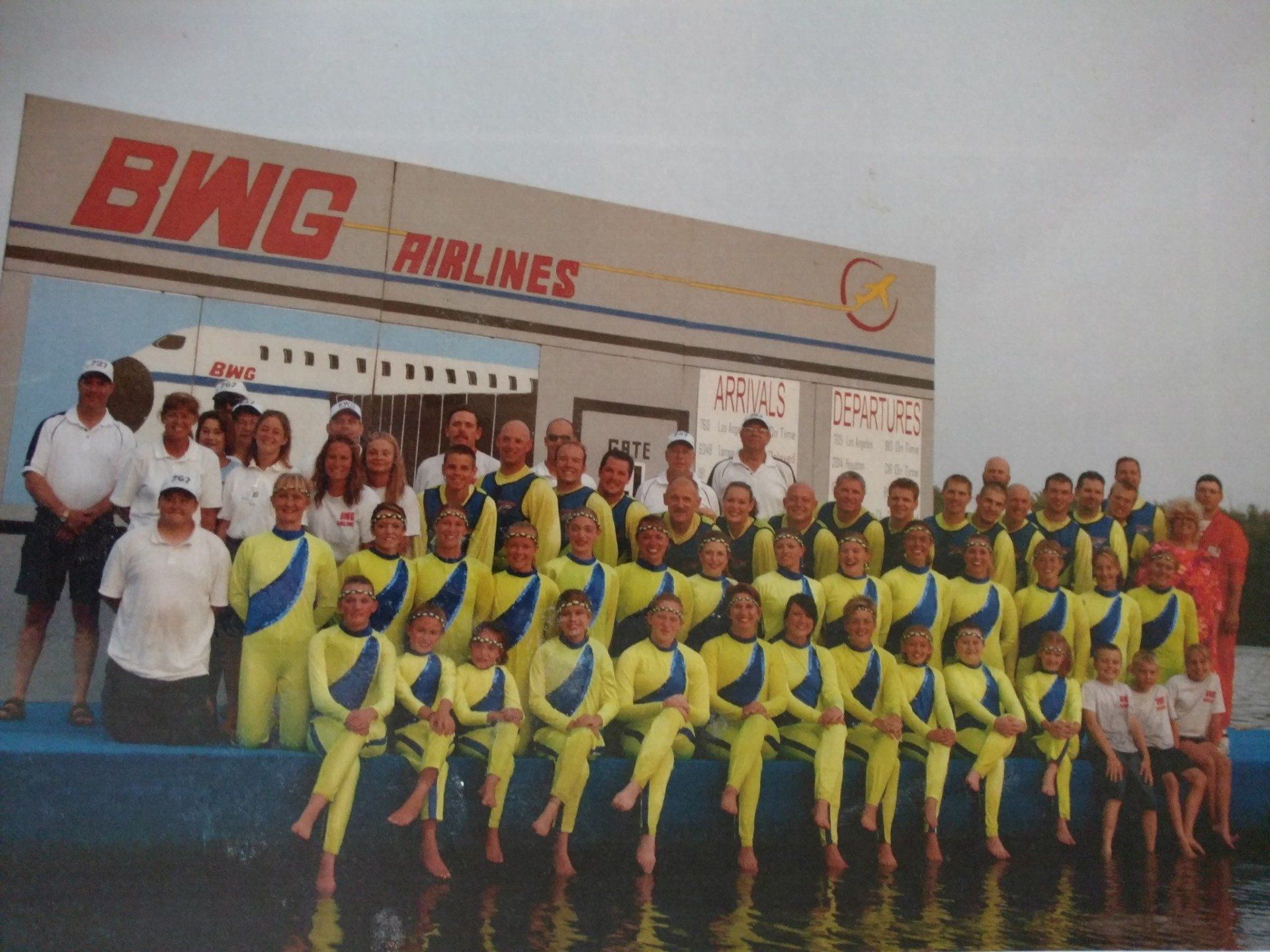 A large group of people are posing in front of a building that says BWG Airlines