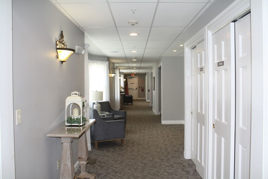 Long hallway with gray walls, white doors, carpeted floor, and a chair with a lamp on a small table.