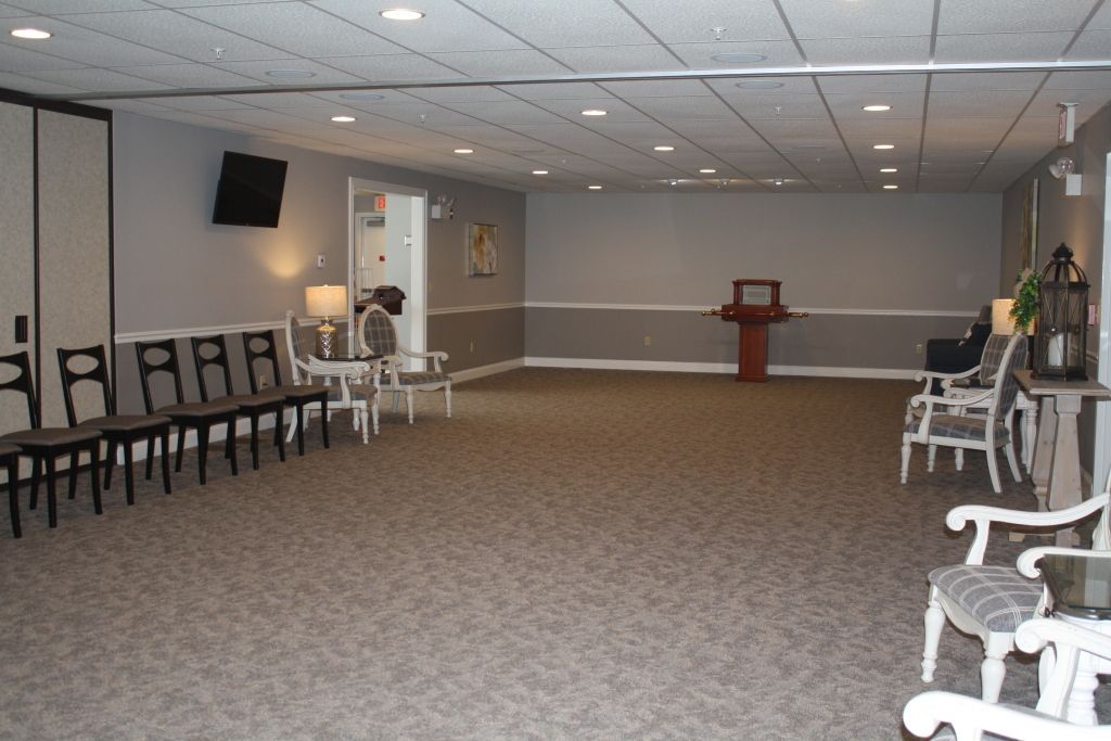 Empty banquet hall with rows of chairs, white rocking chairs, and a podium at the far end.