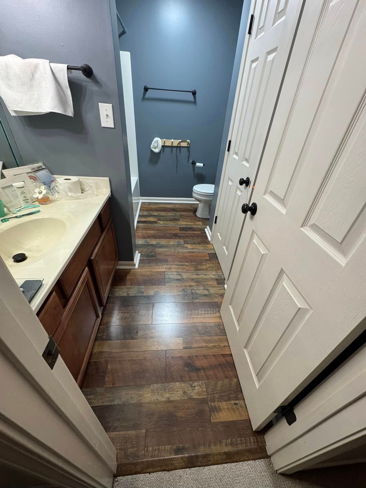 Bathroom with wood-look floor, dark blue walls, toilet, vanity, and a white towel rack.