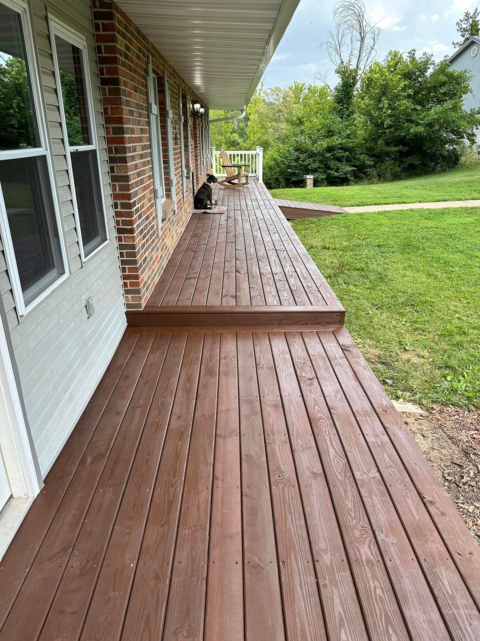A cat is sitting on a wooden deck in front of a house.