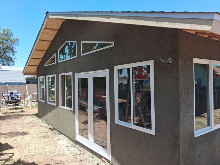 Small brown stucco building with white-framed windows and glass double doors under construction.