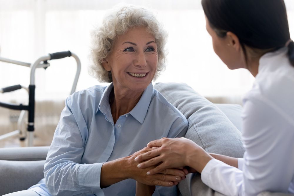 An Elderly Woman is Sitting on a Couch Holding the Hand of a Nurse — Universal Nurse in Toogoolawah, QLD