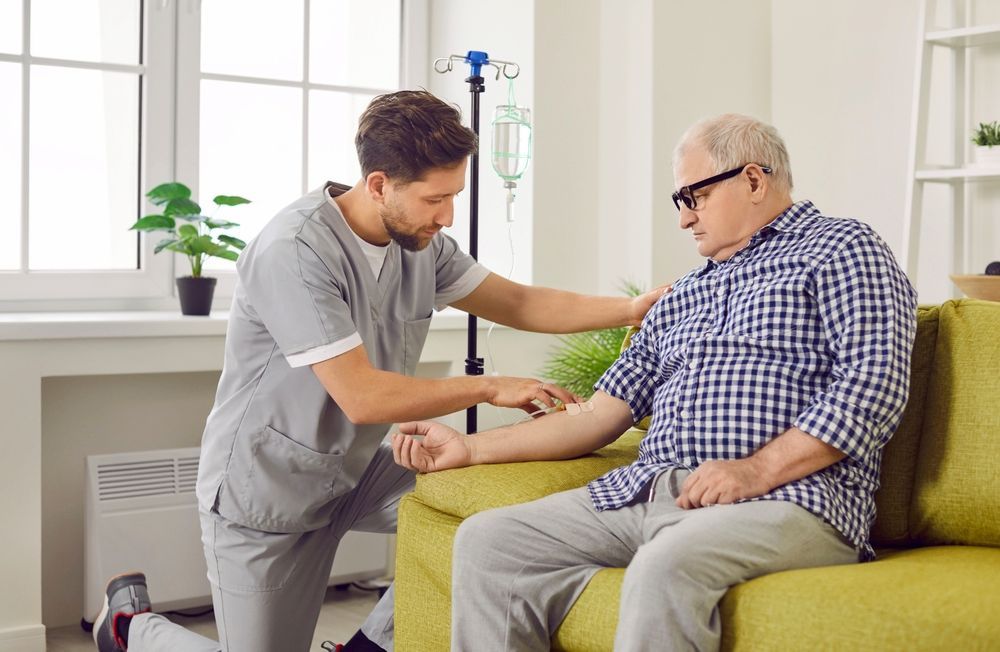 Nurse Placing IV on Senior Man’s Arm on Couch — Universal Nurse in Kilcoy, QLD