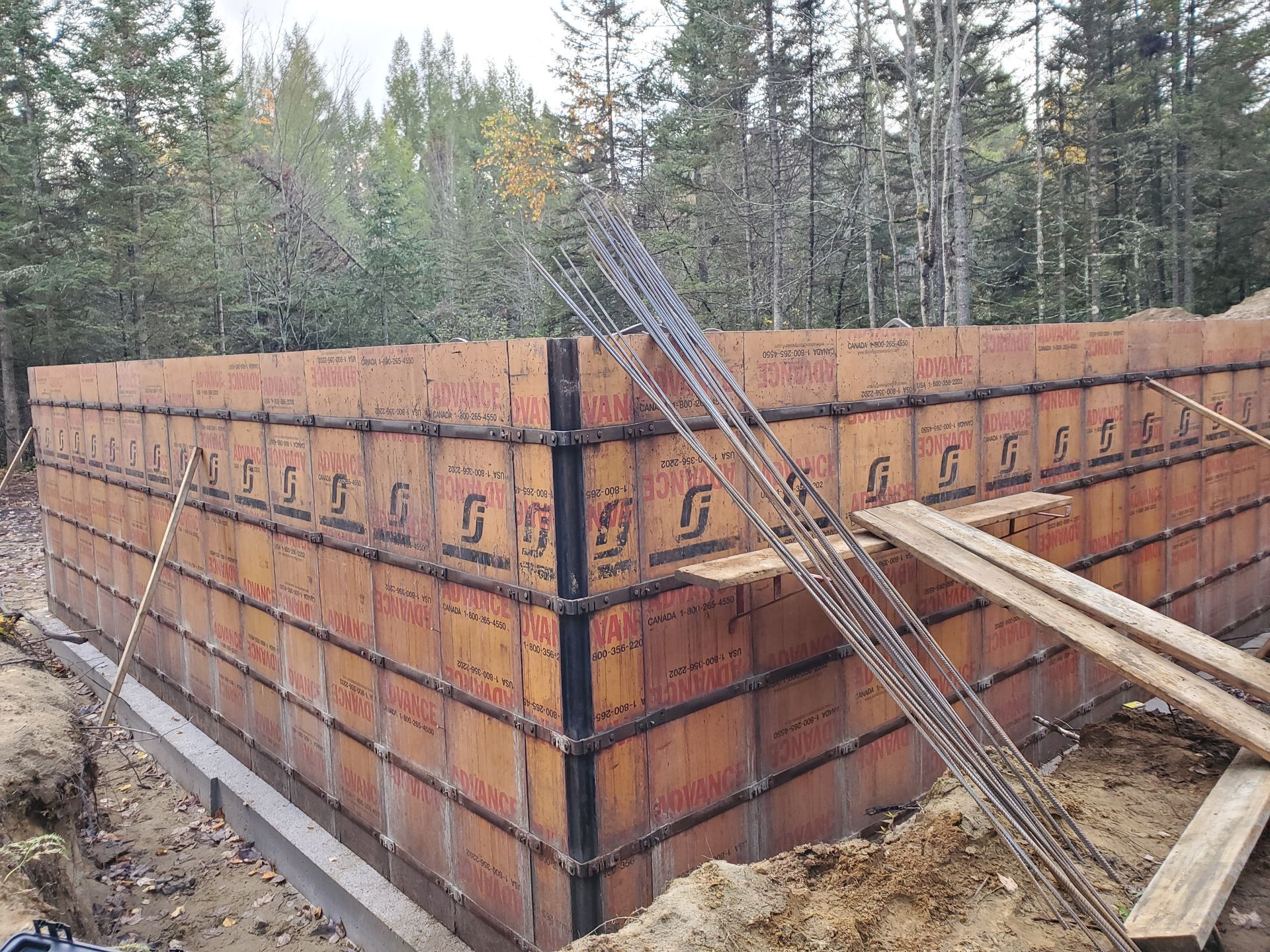 Coffrage en béton brun pour les fondations d'un bâtiment, avec armatures et planches de bois, dans une zone boisée.