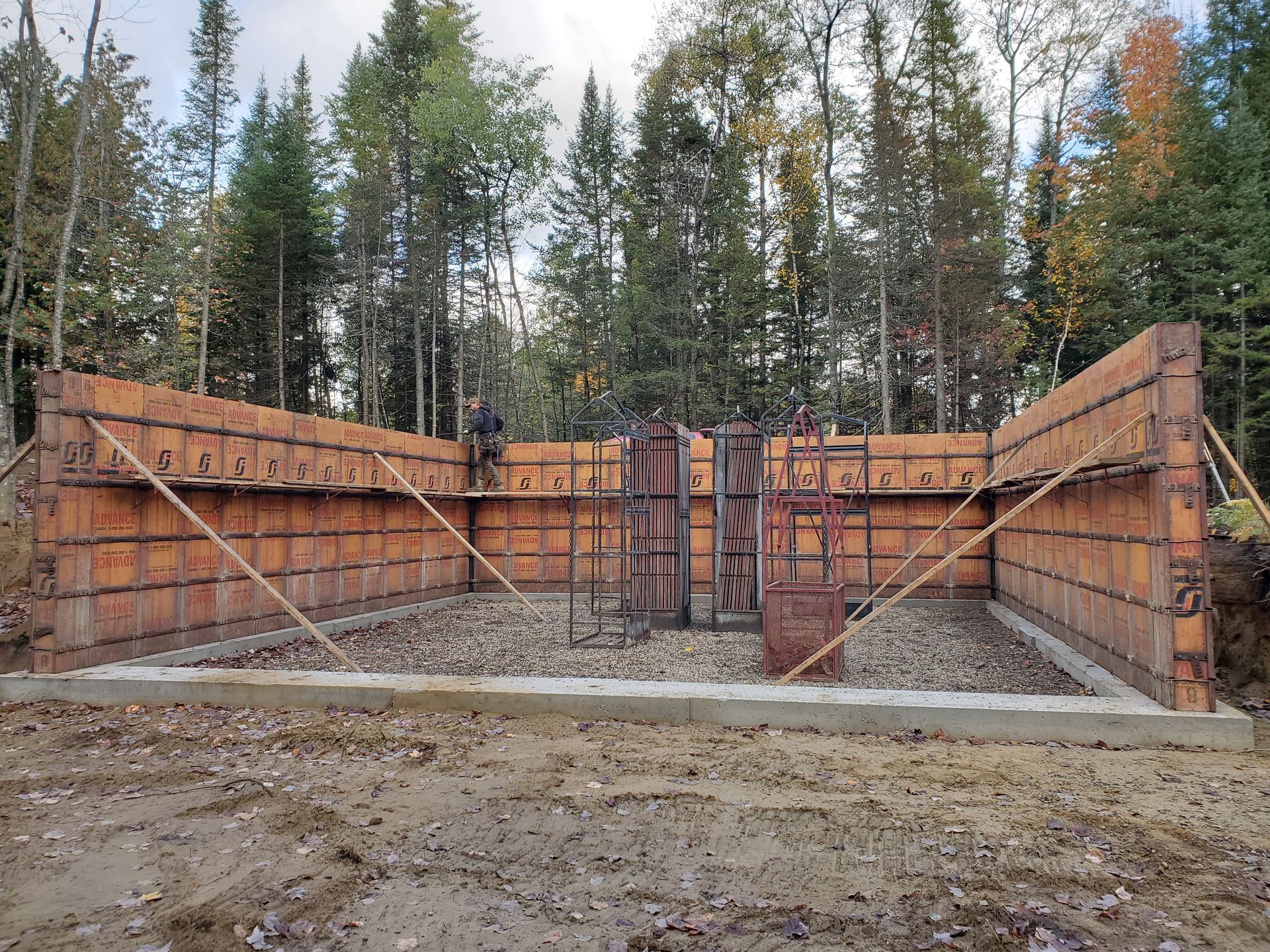 Coffrages en bois pour fondations en béton, avec étais, base de gravier et une personne travaillant.