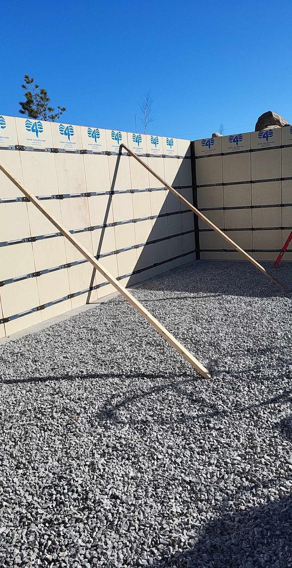 Vue extérieure d'une construction en blocs de coffrage isolant (ICF), soutenue par des supports en bois, sur fond de ciel bleu et de gravier.