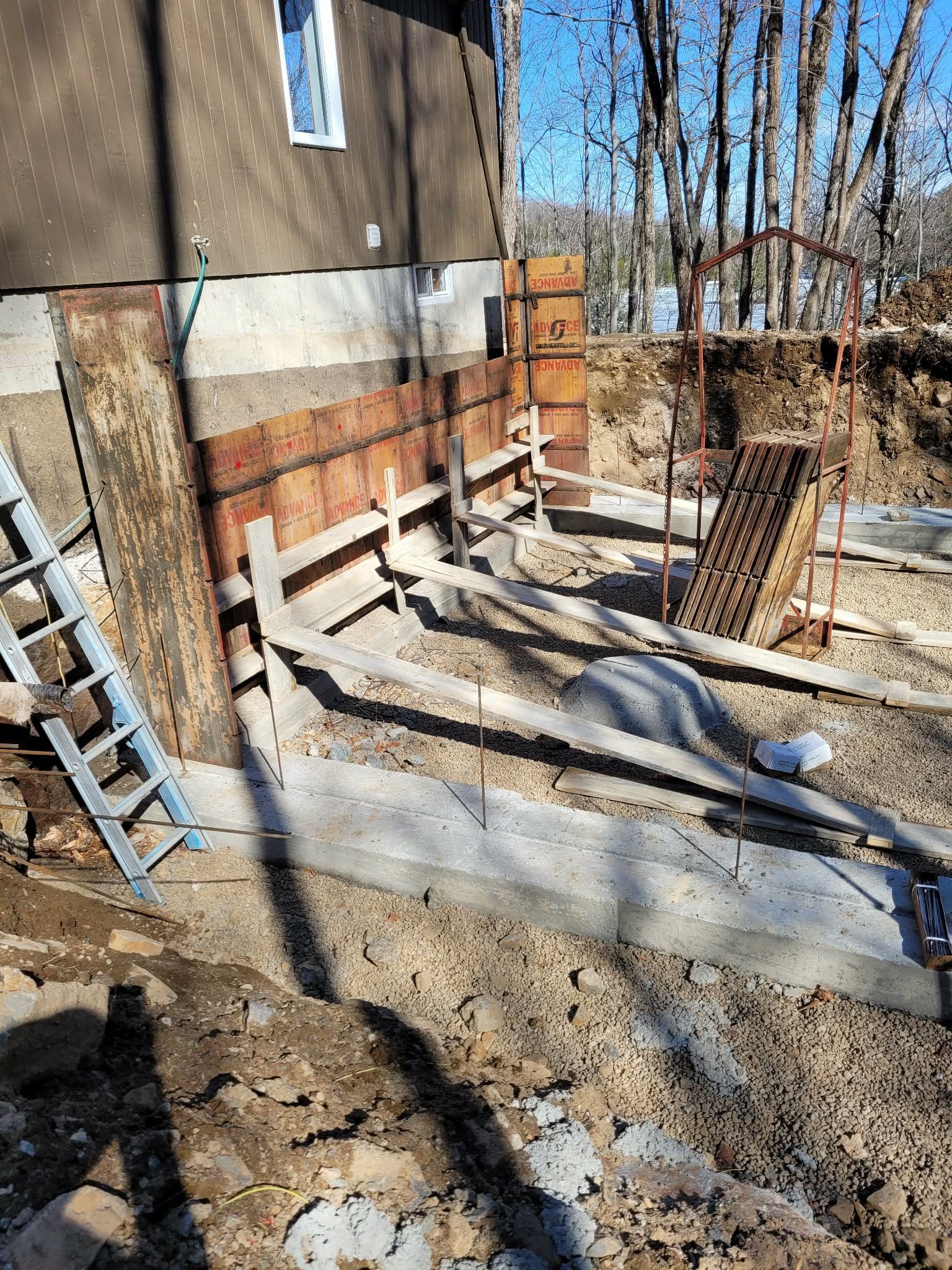 Chantier de construction avec coffrages de fondation et échelle. Vue extérieure d'une maison avec de la terre et des matériaux de construction.