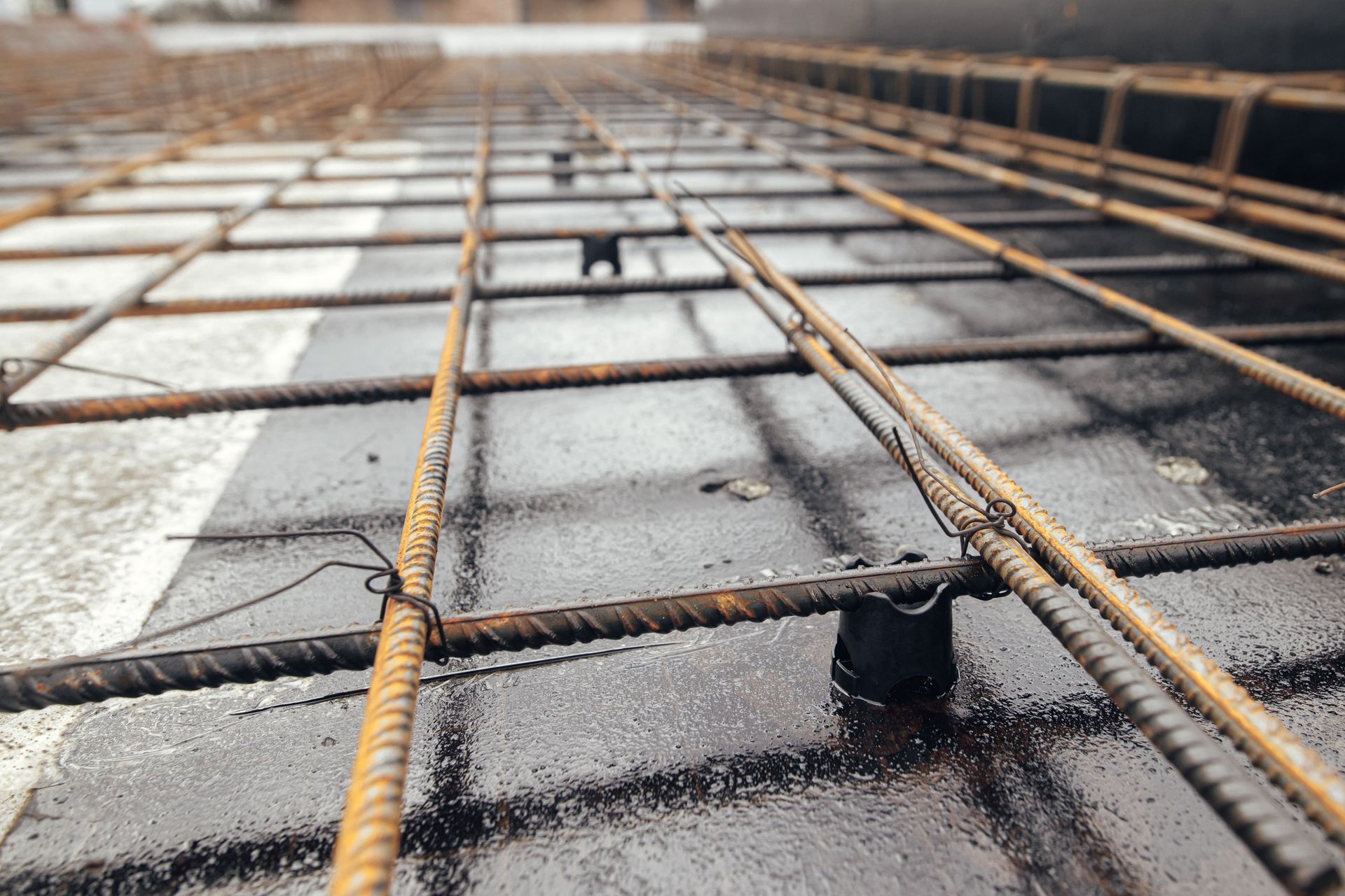 Barres d'acier renforcées, disposées en quadrillage, sur une surface humide, prêtes à recevoir le béton.