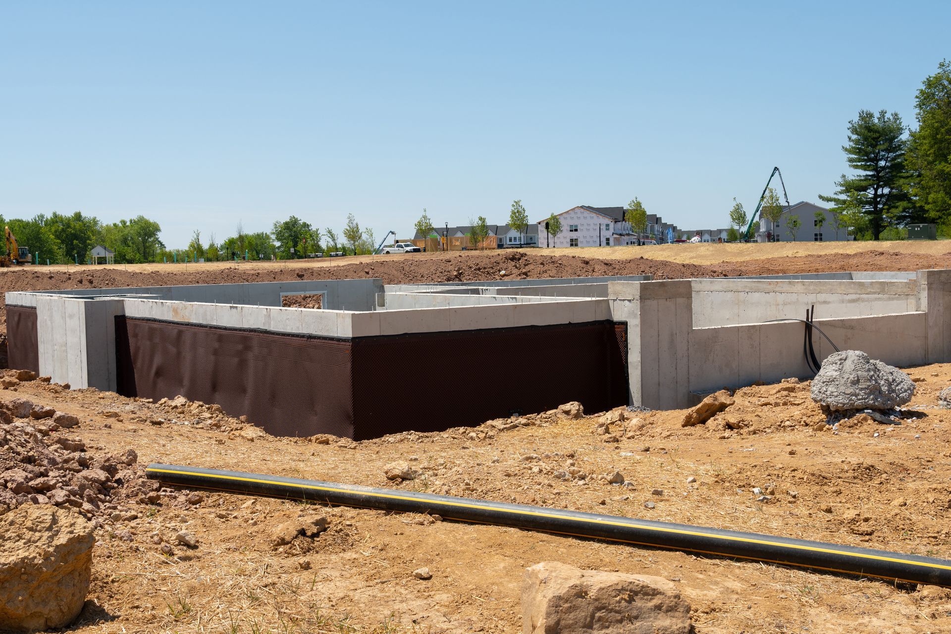 Fondations d'une maison en construction ; murs en béton, couche de protection brune, terre, ciel bleu.