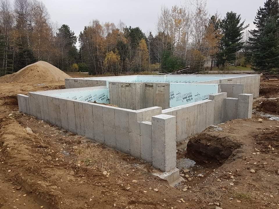 Fondations en béton d'un bâtiment en construction, posées sur la terre, avec isolation bleue visible.