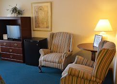 A hotel room with two chairs , a table , a television and a refrigerator.