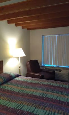 A hotel room with a bed , chair , lamp and window.