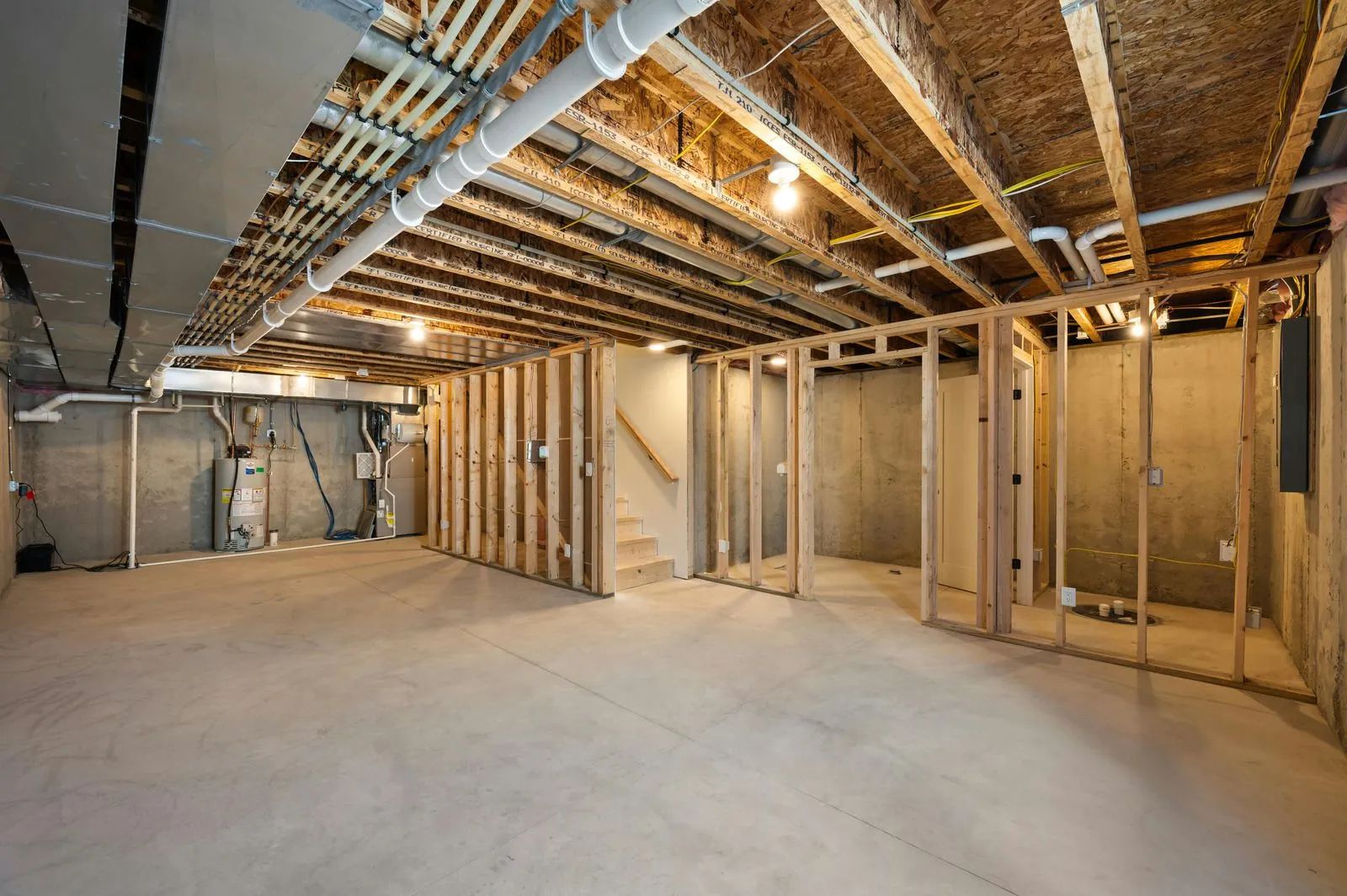 Empty unfinished basement with exposed framing, pipes, and concrete floor