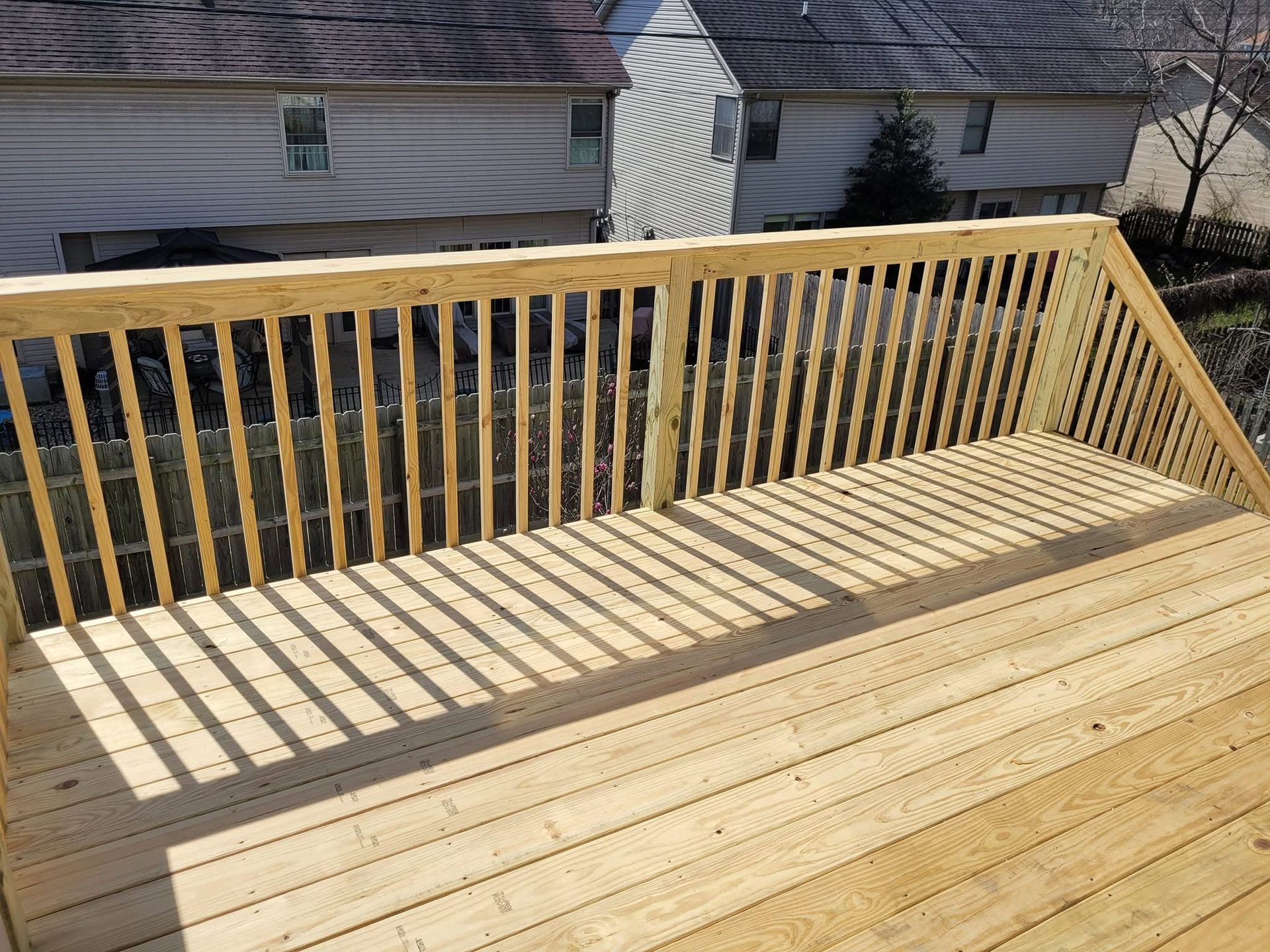 Wooden deck with a railing, viewed from above, overlooking neighboring houses and yards.