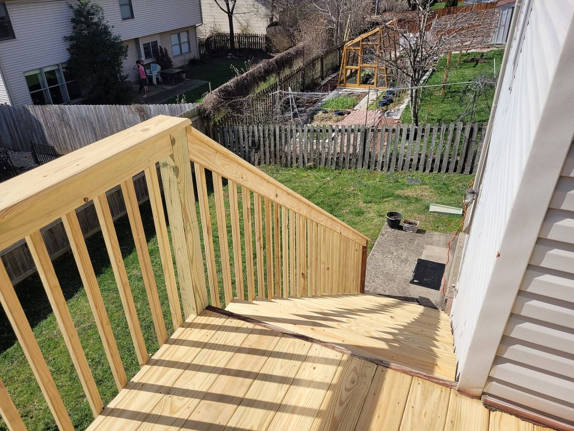 Wooden outdoor staircase with railing leading down to a backyard and neighboring houses in sunlight