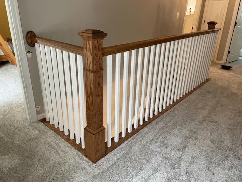Indoor staircase corner with white balusters, wood railing, and carpeted floor