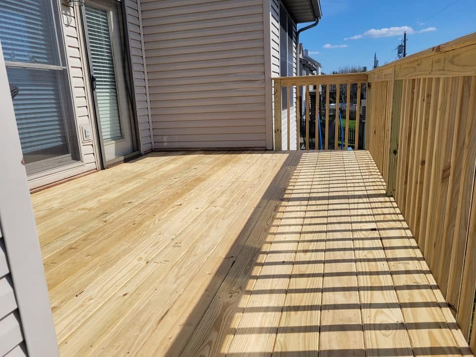 New wooden deck beside a house, with sunlight casting fence shadows across the boards.