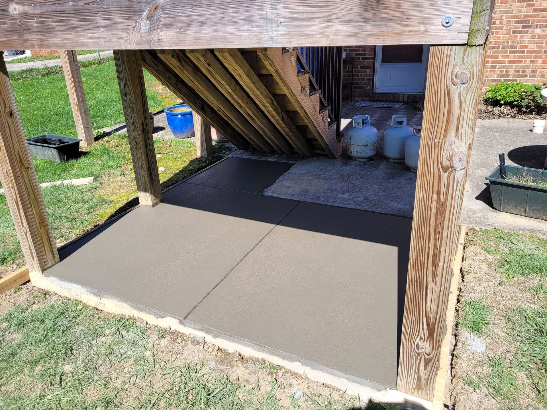Concrete slab beneath outdoor wooden stairs in a backyard storage area