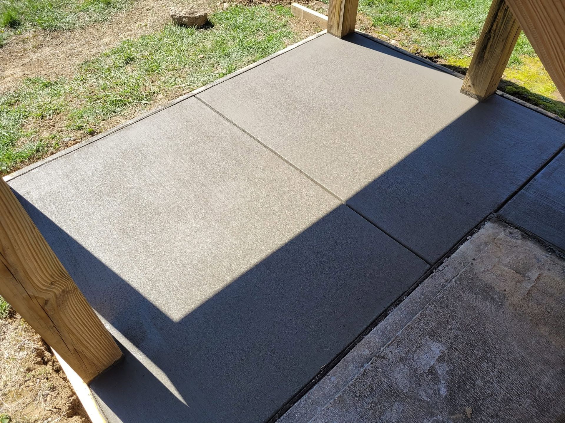 Concrete wheelchair ramp with wooden posts and shadowed landing outdoors