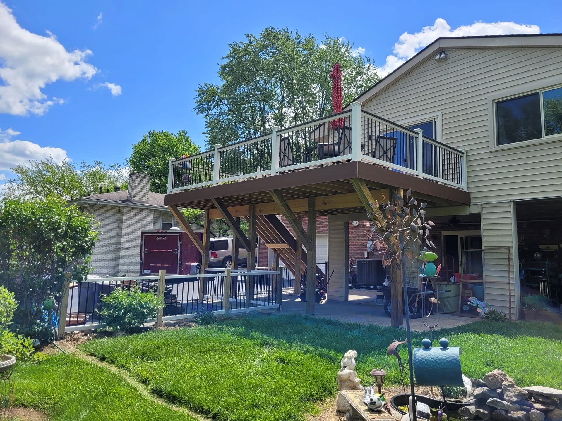 Backyard deck with stairs, patio furniture, and green lawn under a bright blue sky