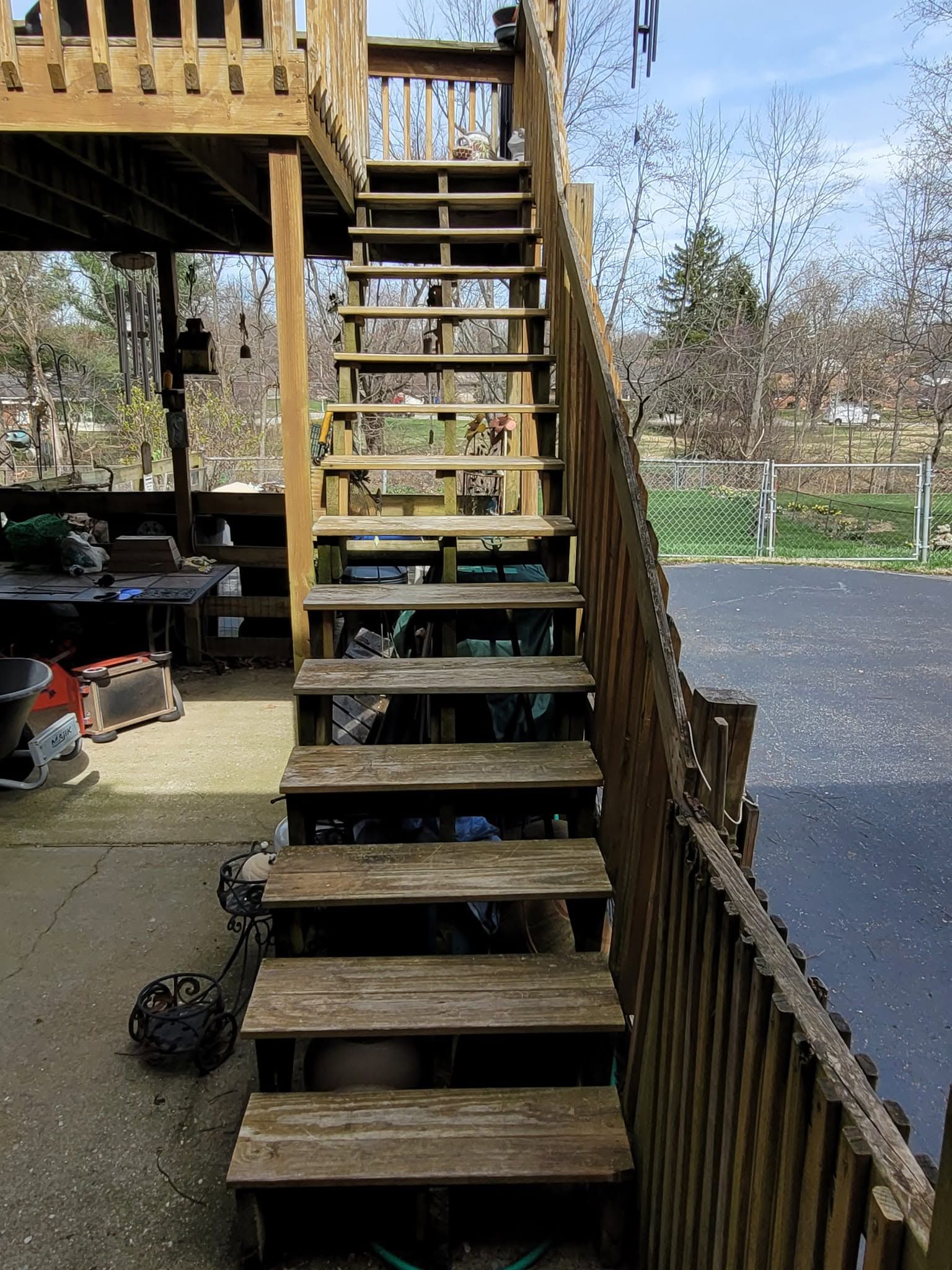 Wooden outdoor staircase beside a deck, with a paved driveway and yard in the background.