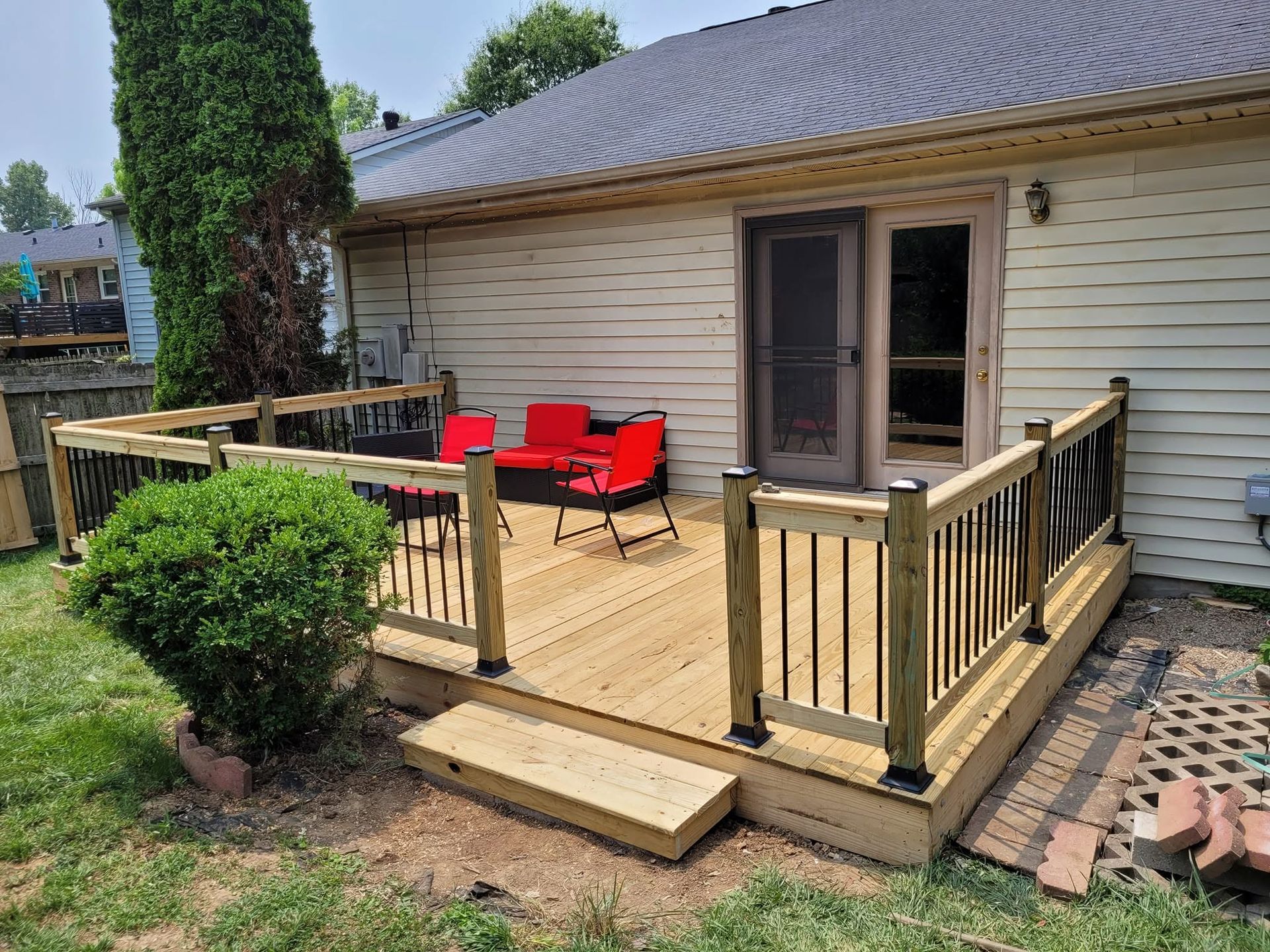 Small wooden deck with red chairs and railing beside a beige house and sliding door