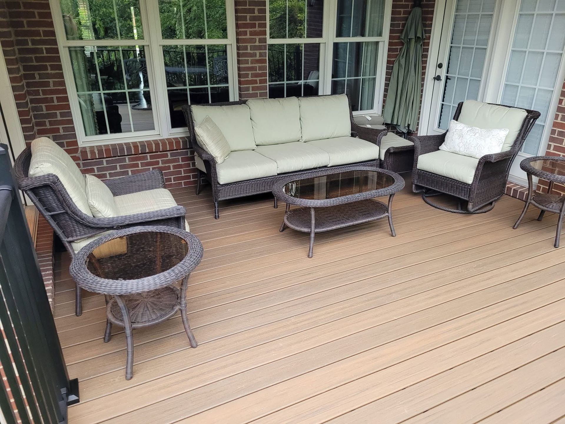 Covered porch with beige outdoor sofa, two chairs, and a glass-top coffee table on a wood deck.