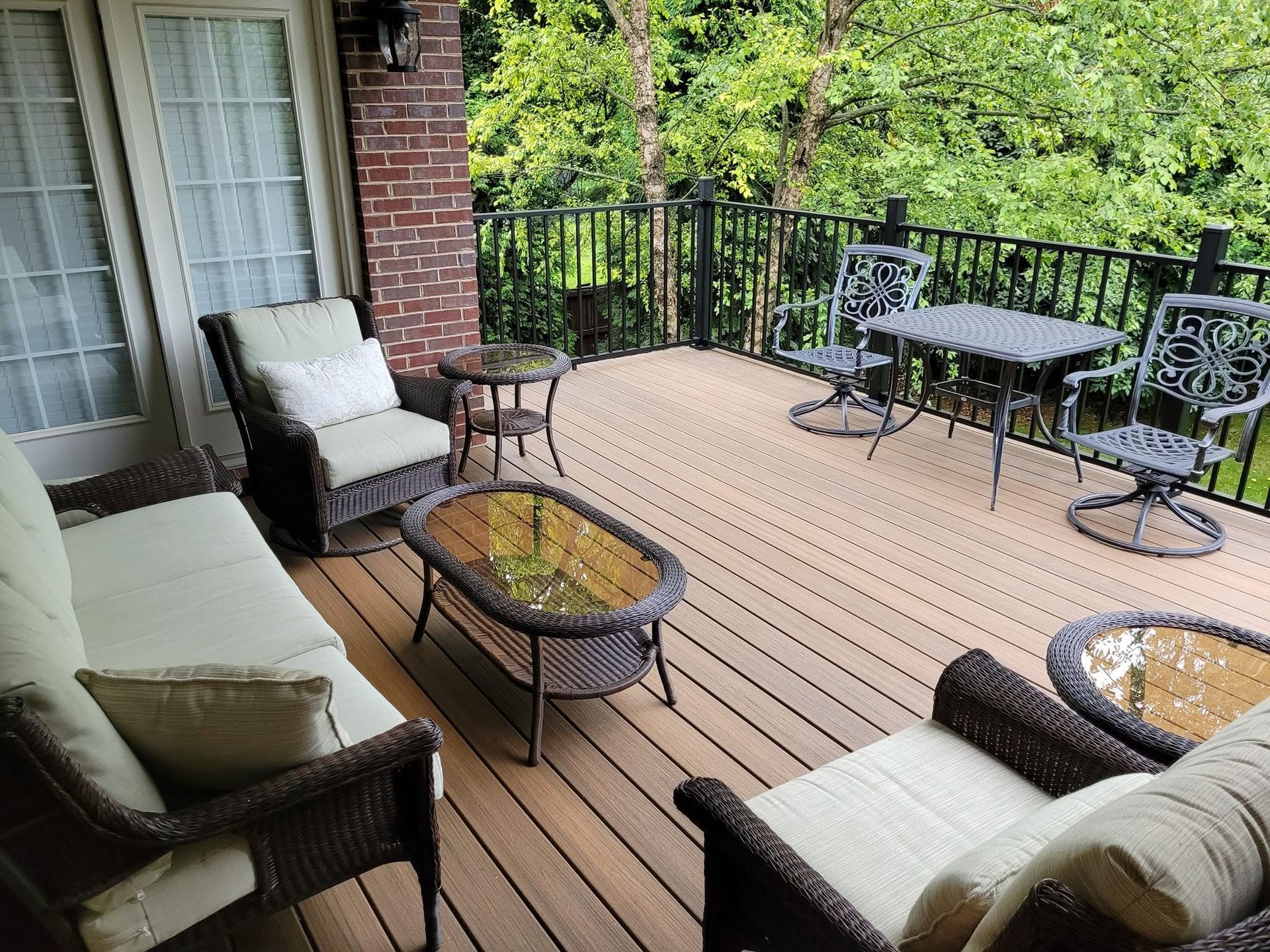 Brick patio with wicker chairs, glass tables, and cream cushions beside a house and trees