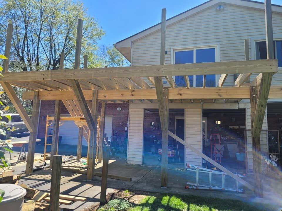 Backyard deck under construction beside a white house, with wooden framing and posts in bright daylight