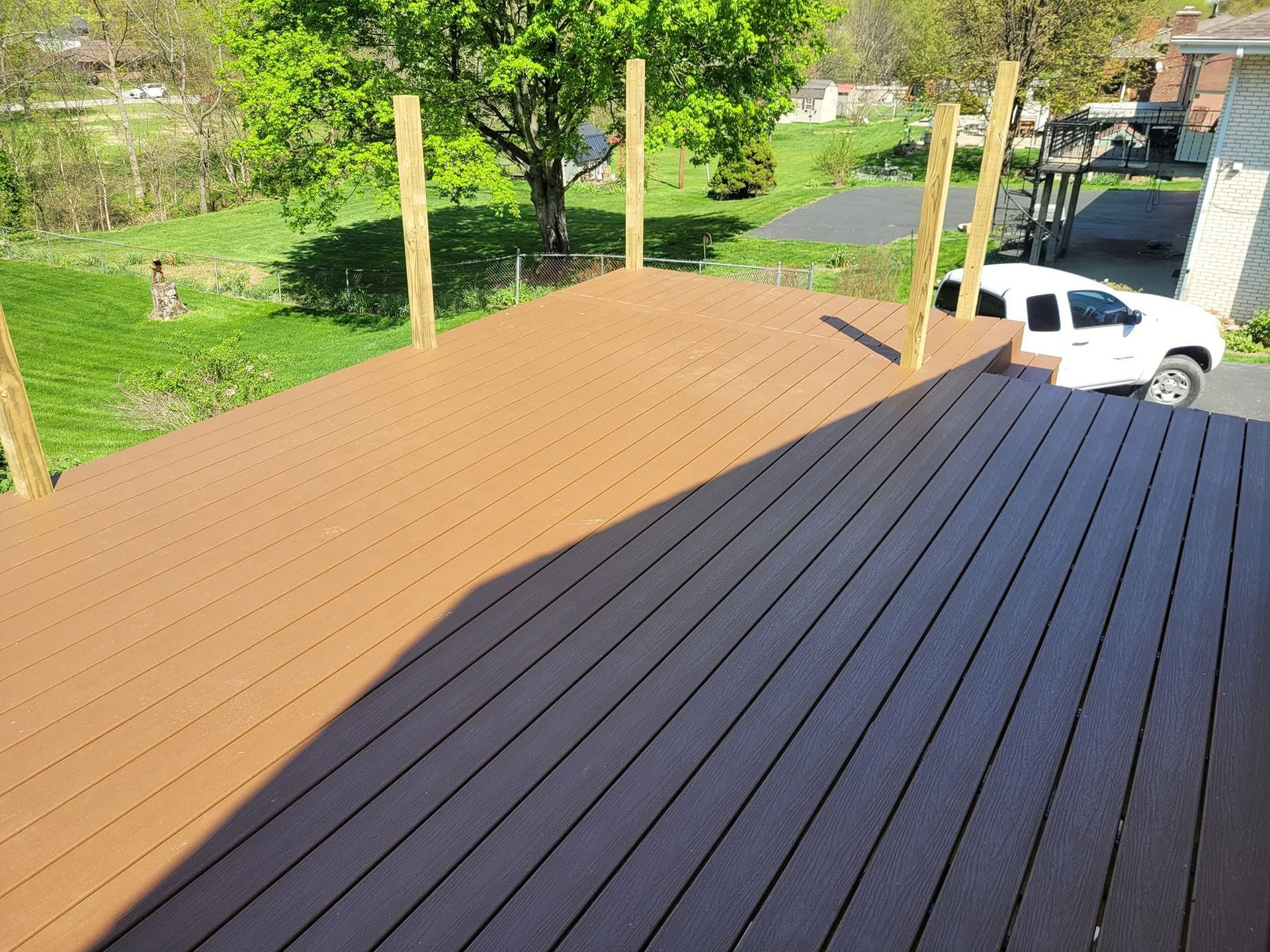 Wooden rooftop deck under construction beside a white van, with posts and a green yard in the background