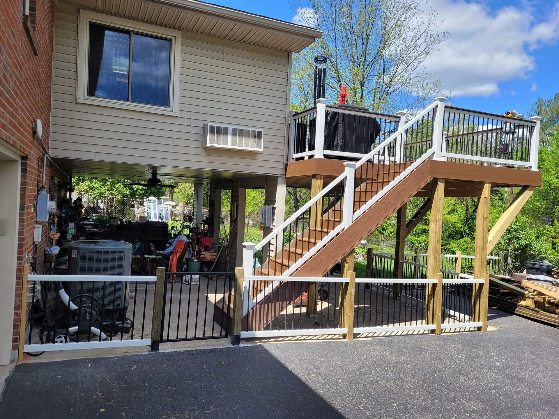 Brick house with raised deck, stairs, and fenced patio above a driveway
