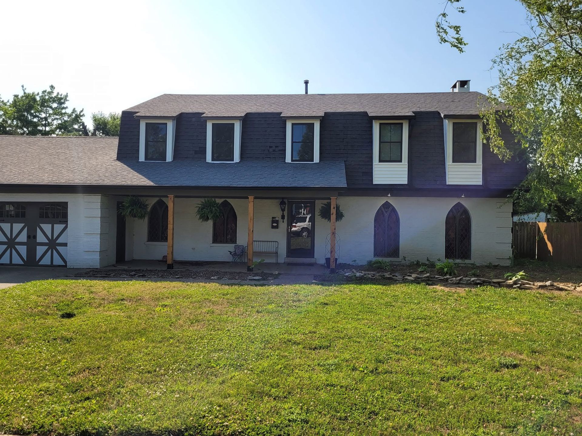 Two-story white house with dark roof, dormer windows, and a grassy front yard in daylight