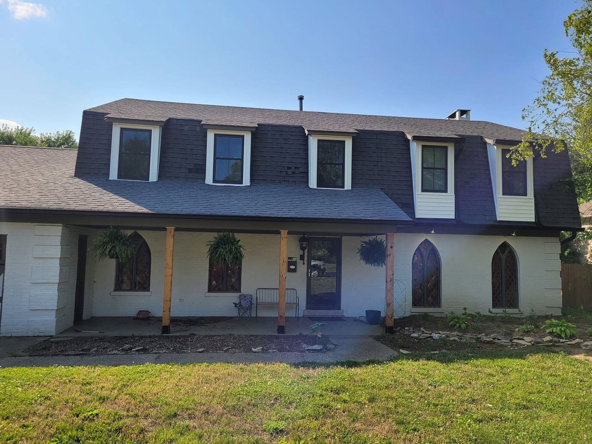 Two-story white house with dark roof, dormer windows, and a covered front porch in a sunny yard