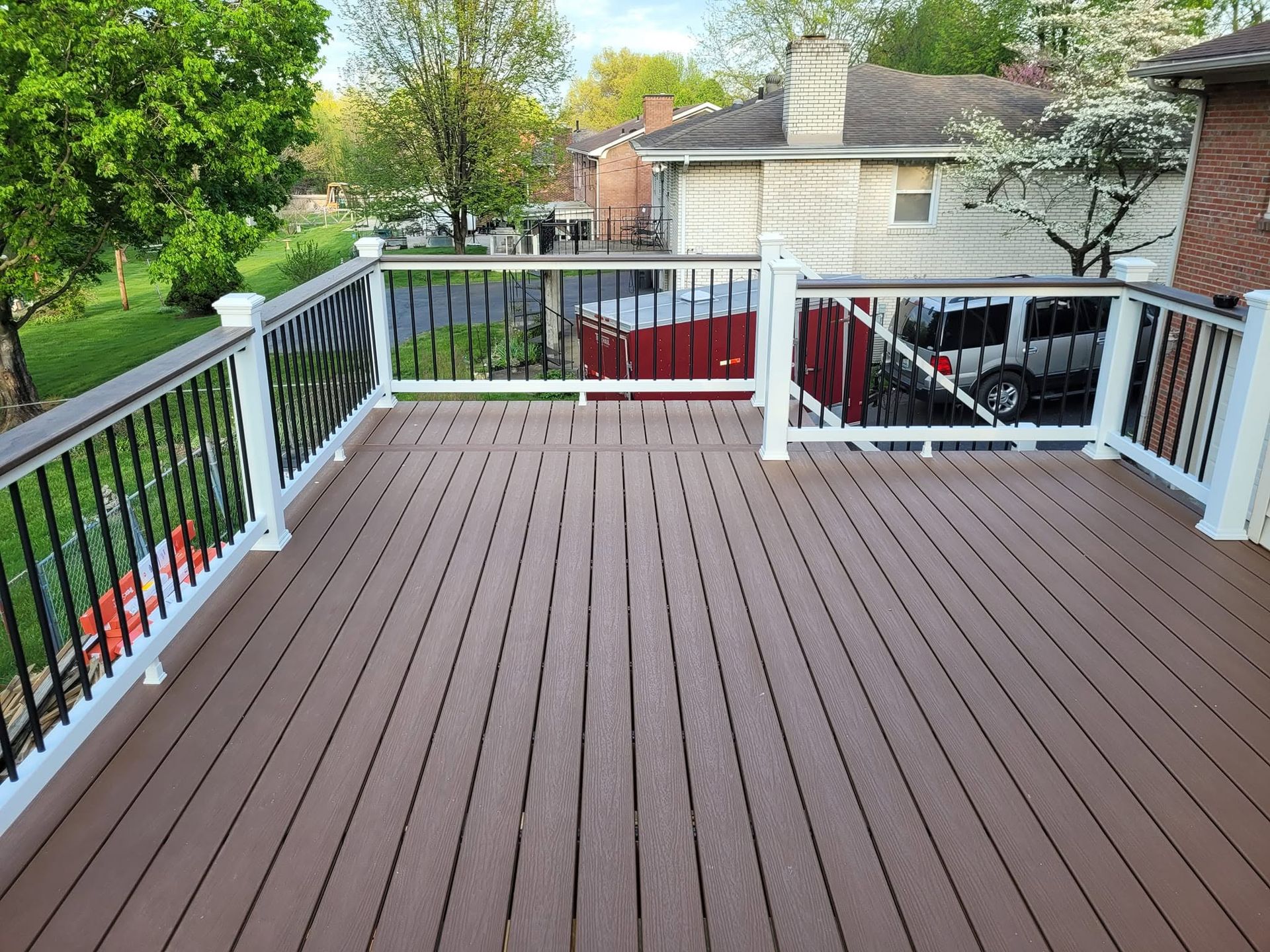 Wooden backyard deck with gray railing and black balusters overlooking neighboring homes and trees