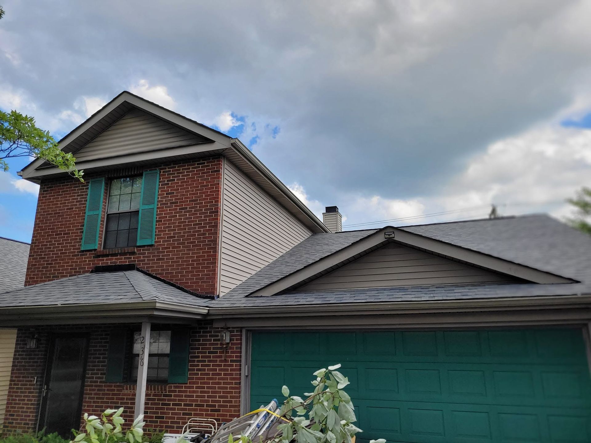 Suburban brick house with teal garage door and cloudy sky