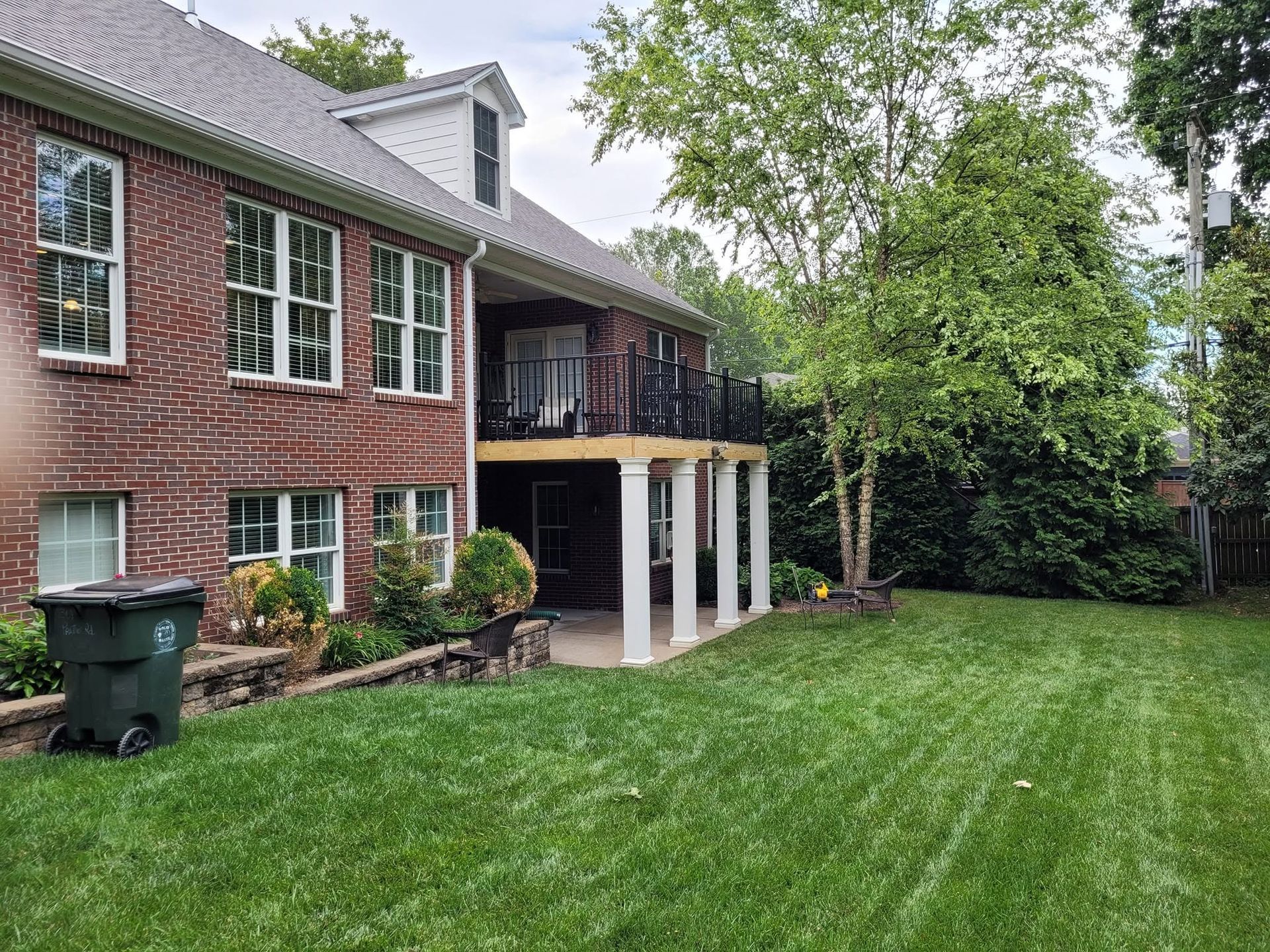 Brick house with white columns and large green lawn, viewed from the backyard