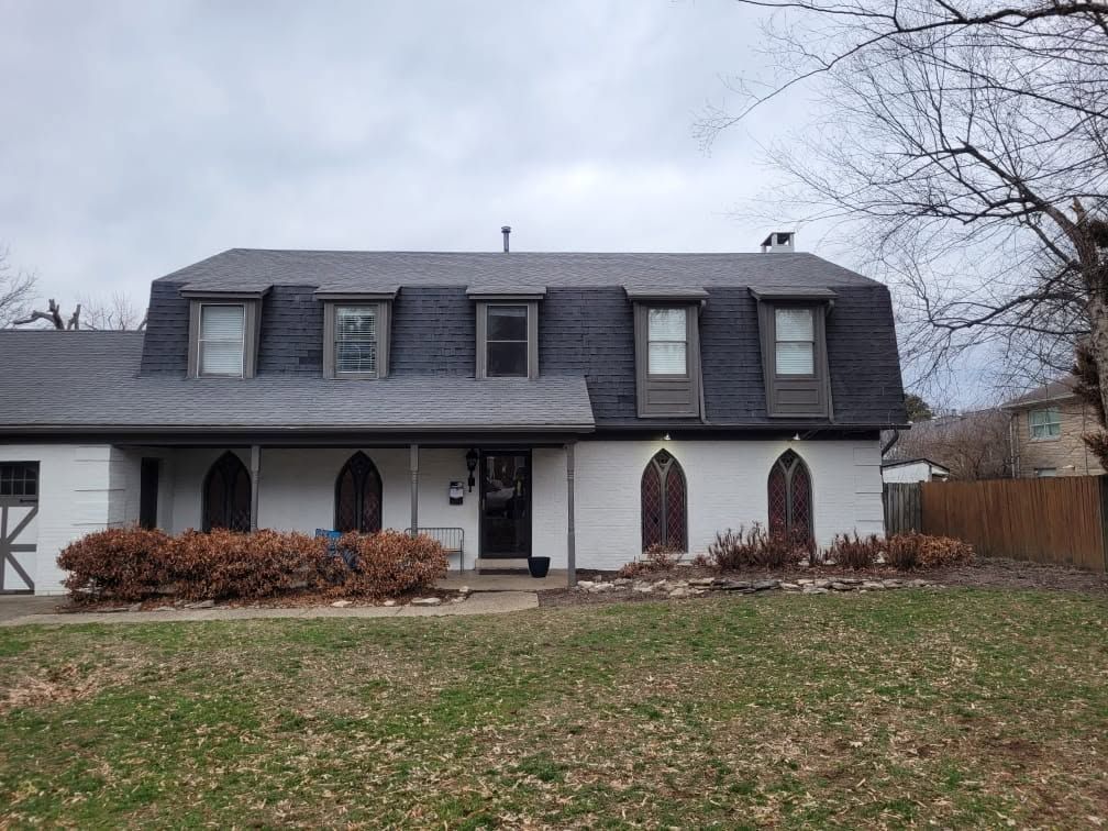 Two-story gray house with dormer windows and a front lawn on an overcast day