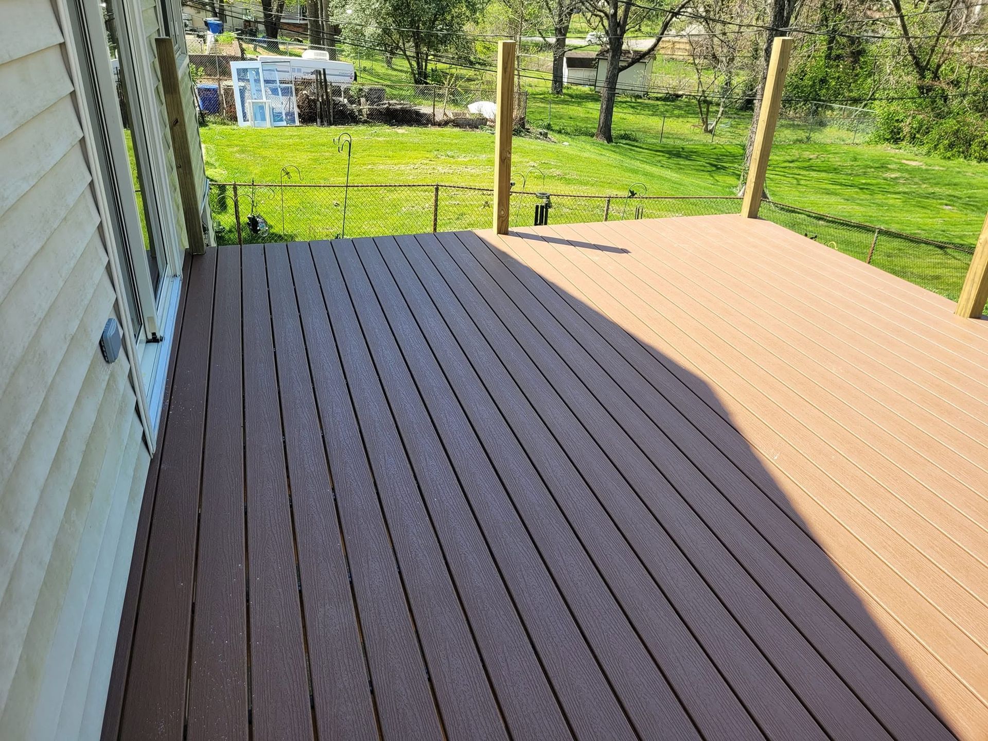Wooden deck beside a house, overlooking a grassy yard with trees and a parked vehicle.