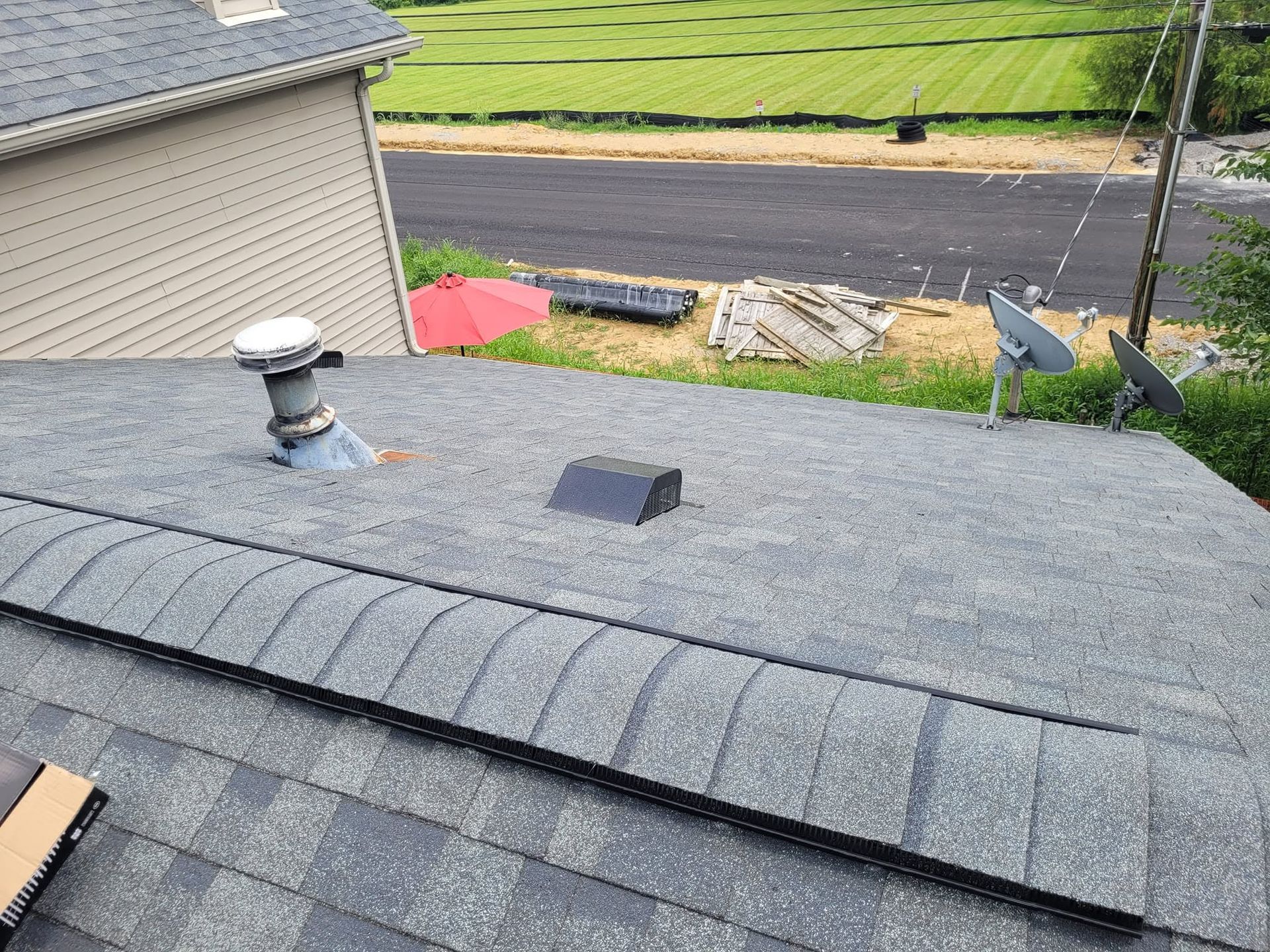 Roof with gray shingles and vents, overlooking a road and grassy landscape beyond.