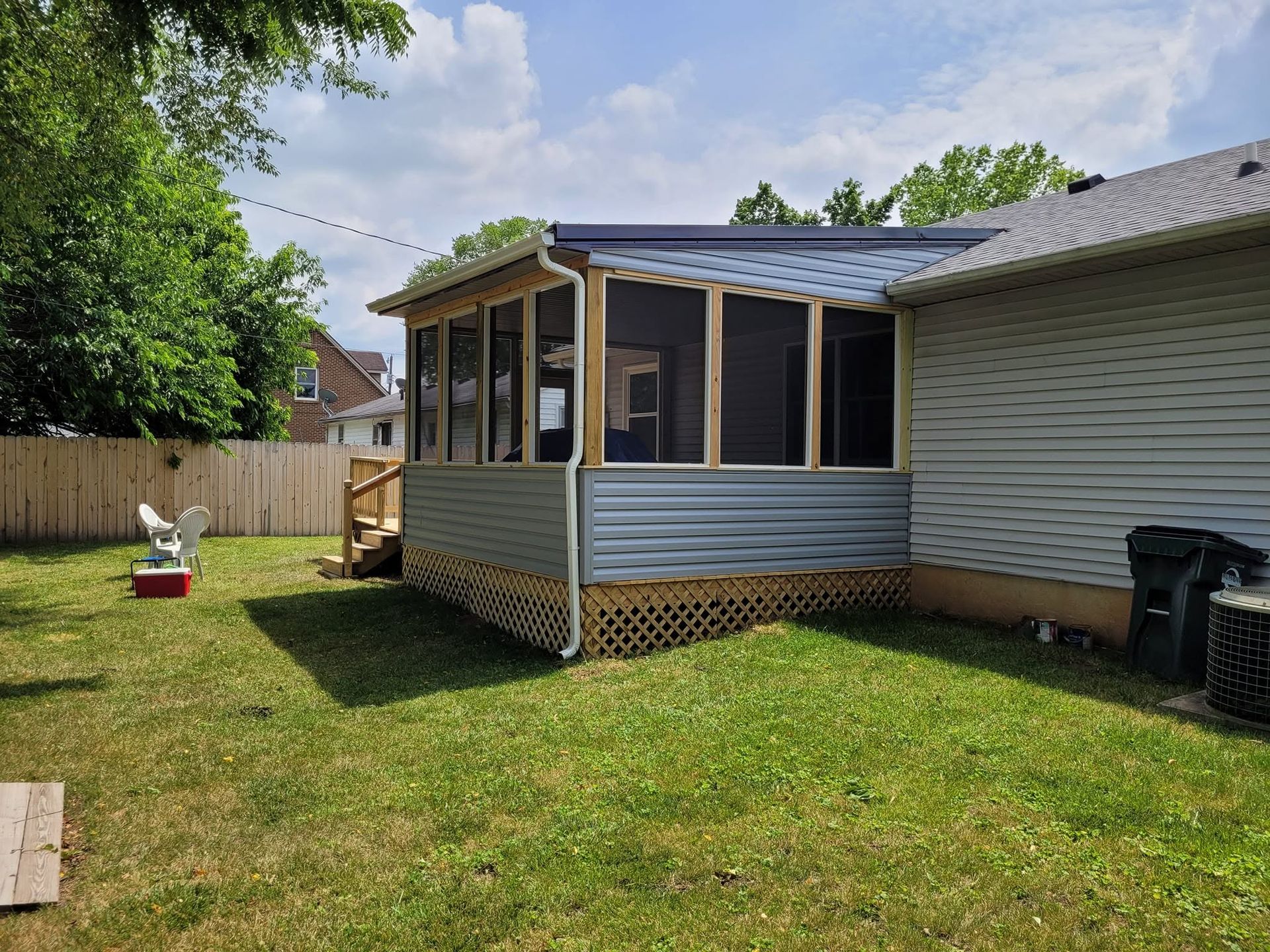 Backyard with screened porch attached to a house, green lawn, wooden fence, and a small playset.