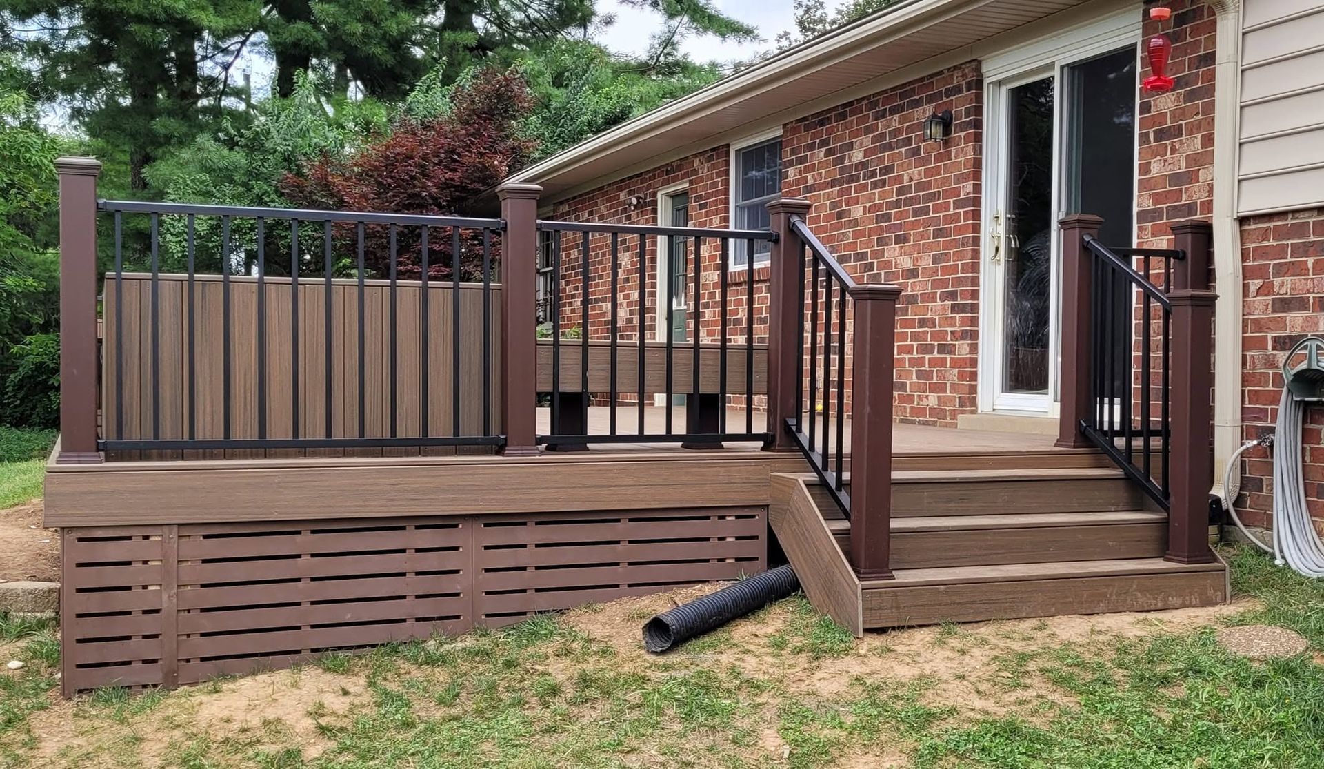 Brick house porch with wooden ramp, steps, and black railing in a yard