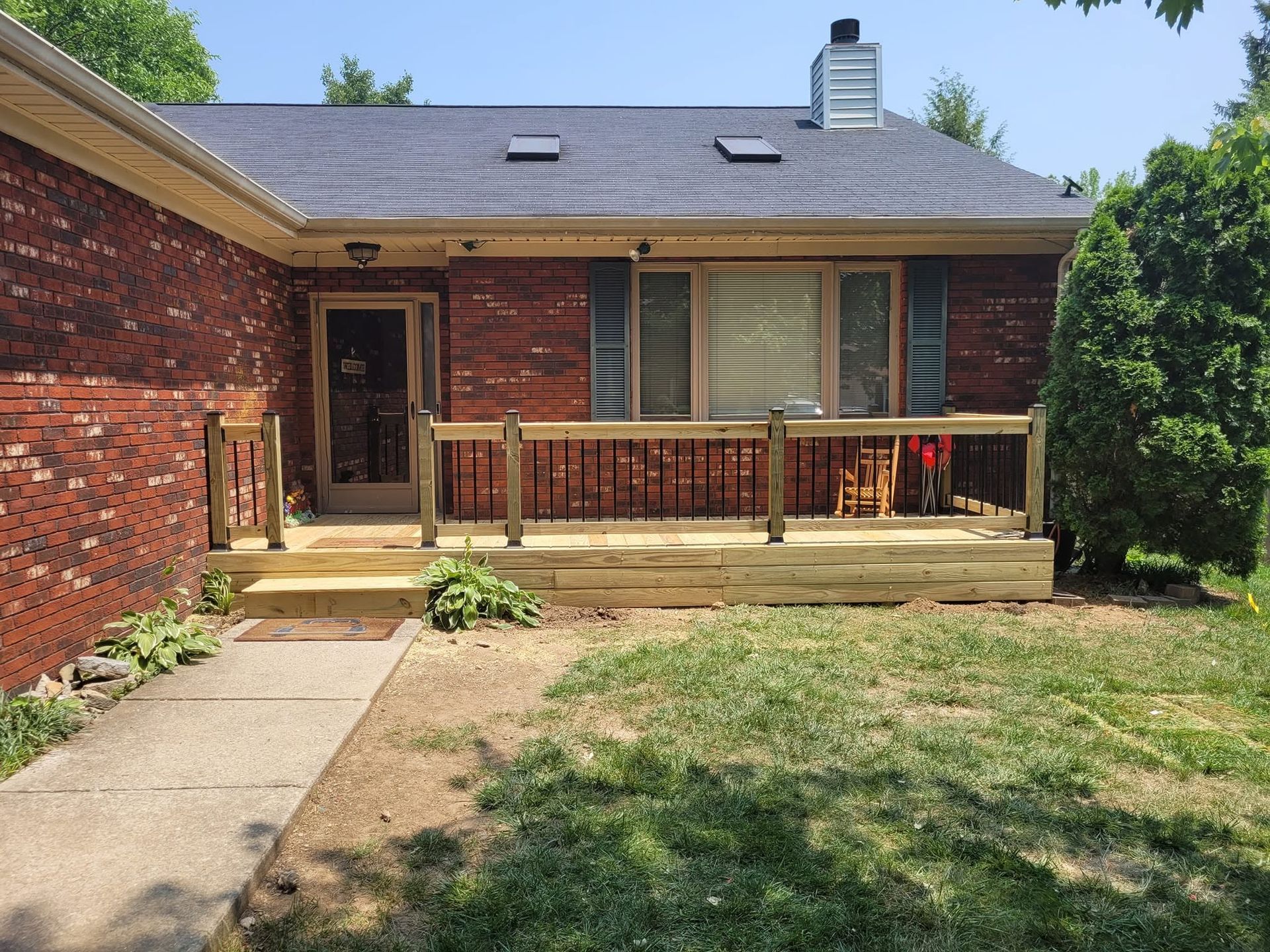 Brick house exterior with covered porch, front walkway, and patchy lawn under a clear sky