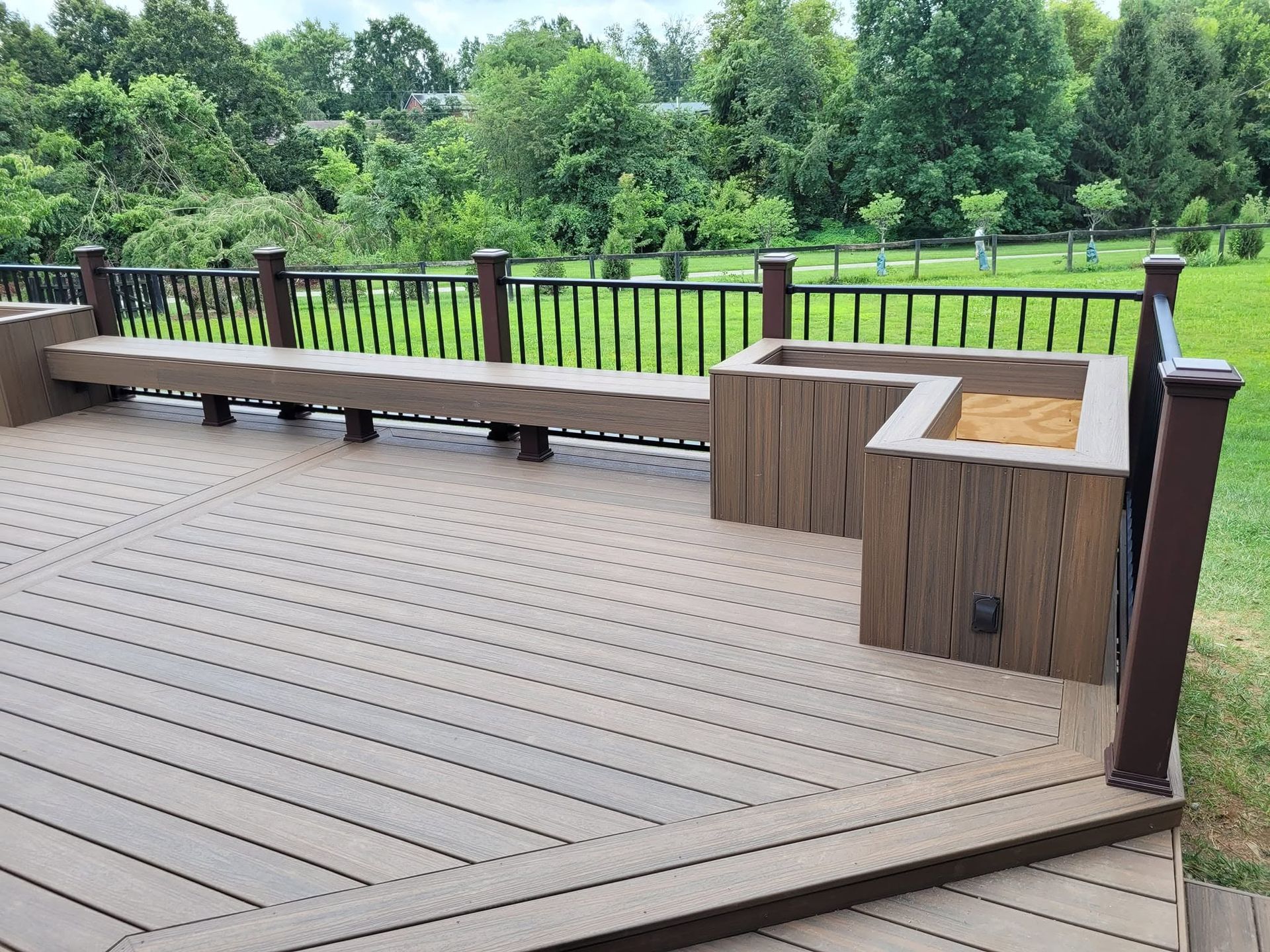 Wooden outdoor deck with benches and railing overlooking a green park and trees.