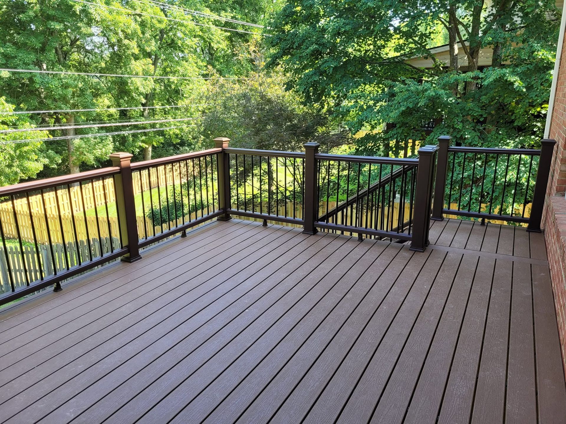 Wooden deck with black railings overlooking a green wooded yard
